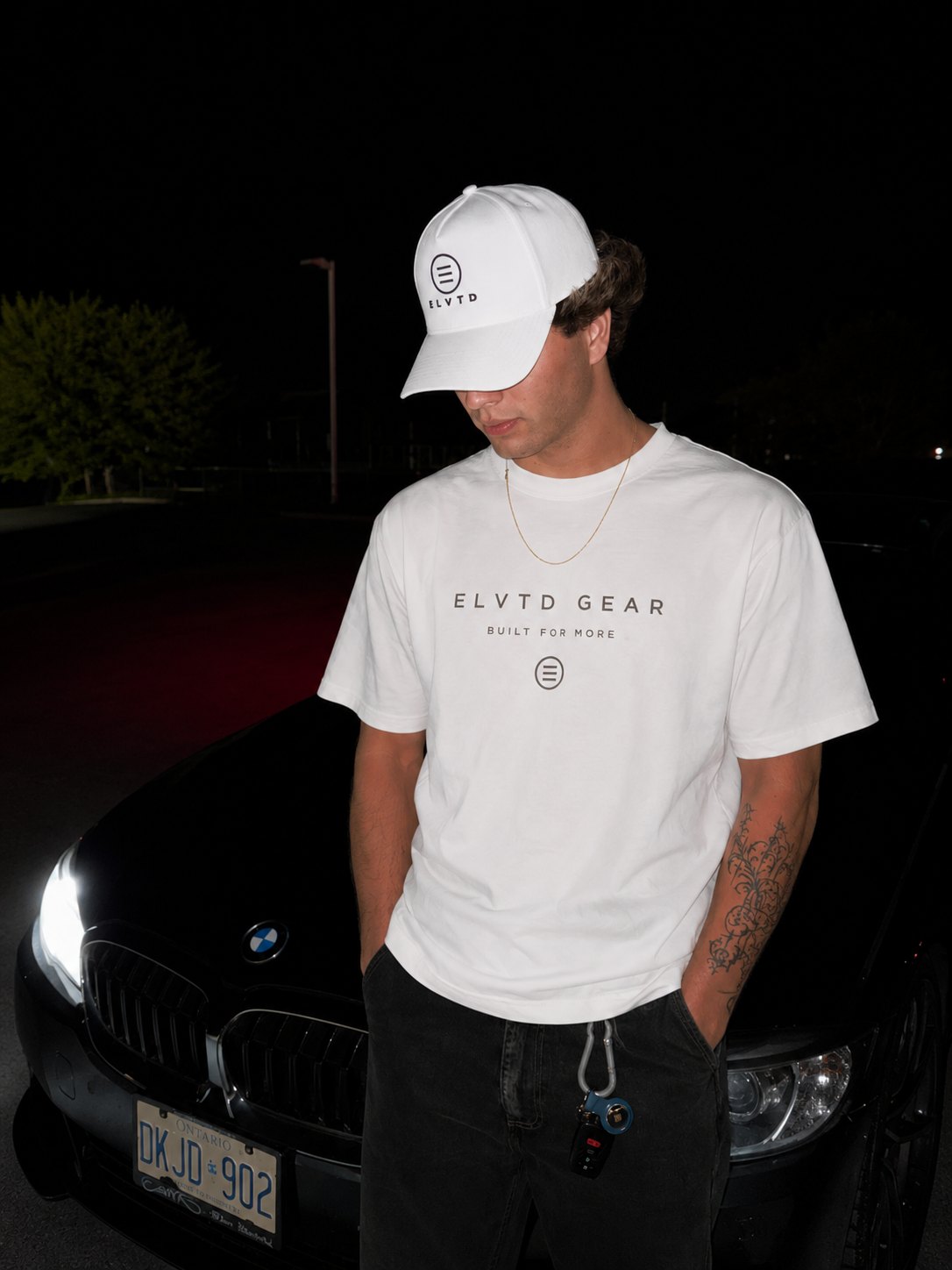 Man in white ELVTD GEAR tee and cap at night